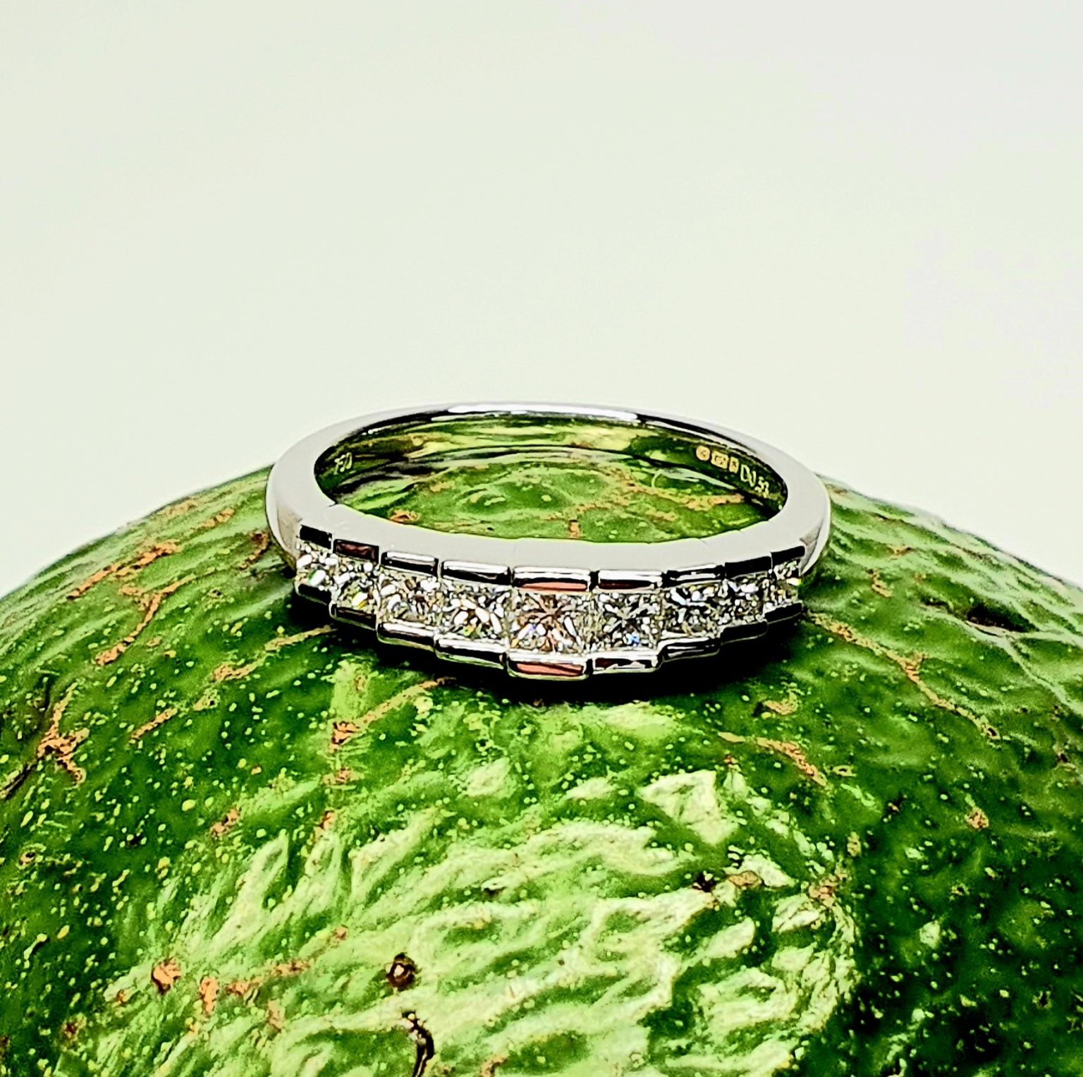Avocado Elegance: The rich green backdrop of an avocado highlights the brilliance of the nine princess-cut diamonds and the polished 18ct white gold, creating a stunning visual contrast.