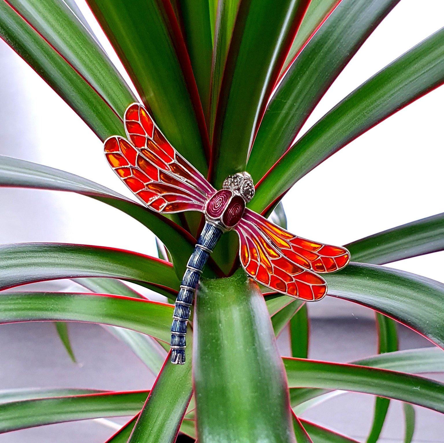 Red dragonfly brooch silver BRS00096- crafted in genuine sterling silver with marcasite eyes inlaid with red, purple & green piqué-a-jour enamel. Pictured perched on a leaf.