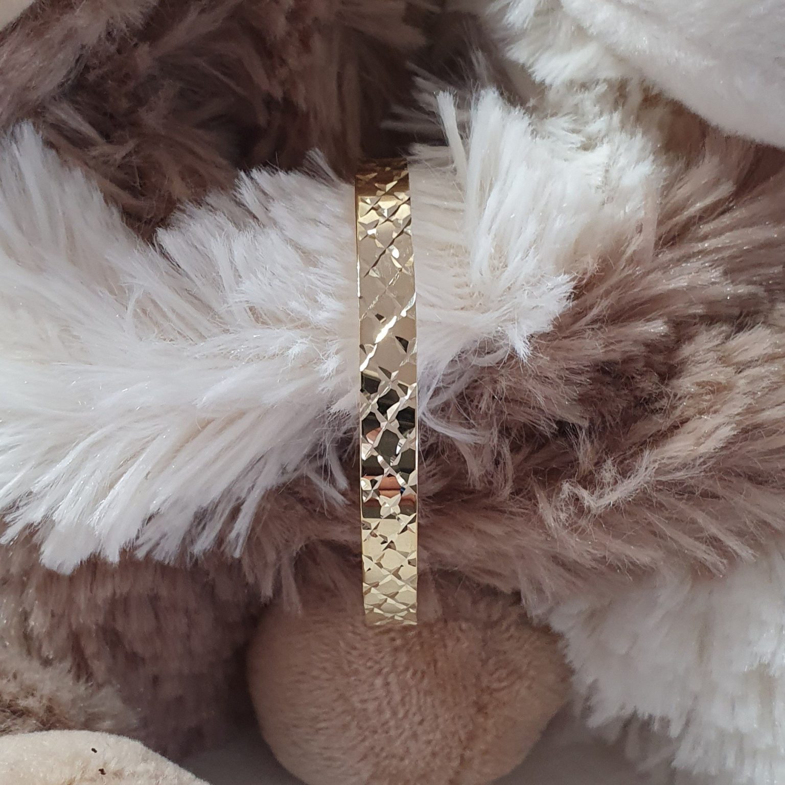 Expanding baby bangle shown in between two cuddling toy teddy bears close up