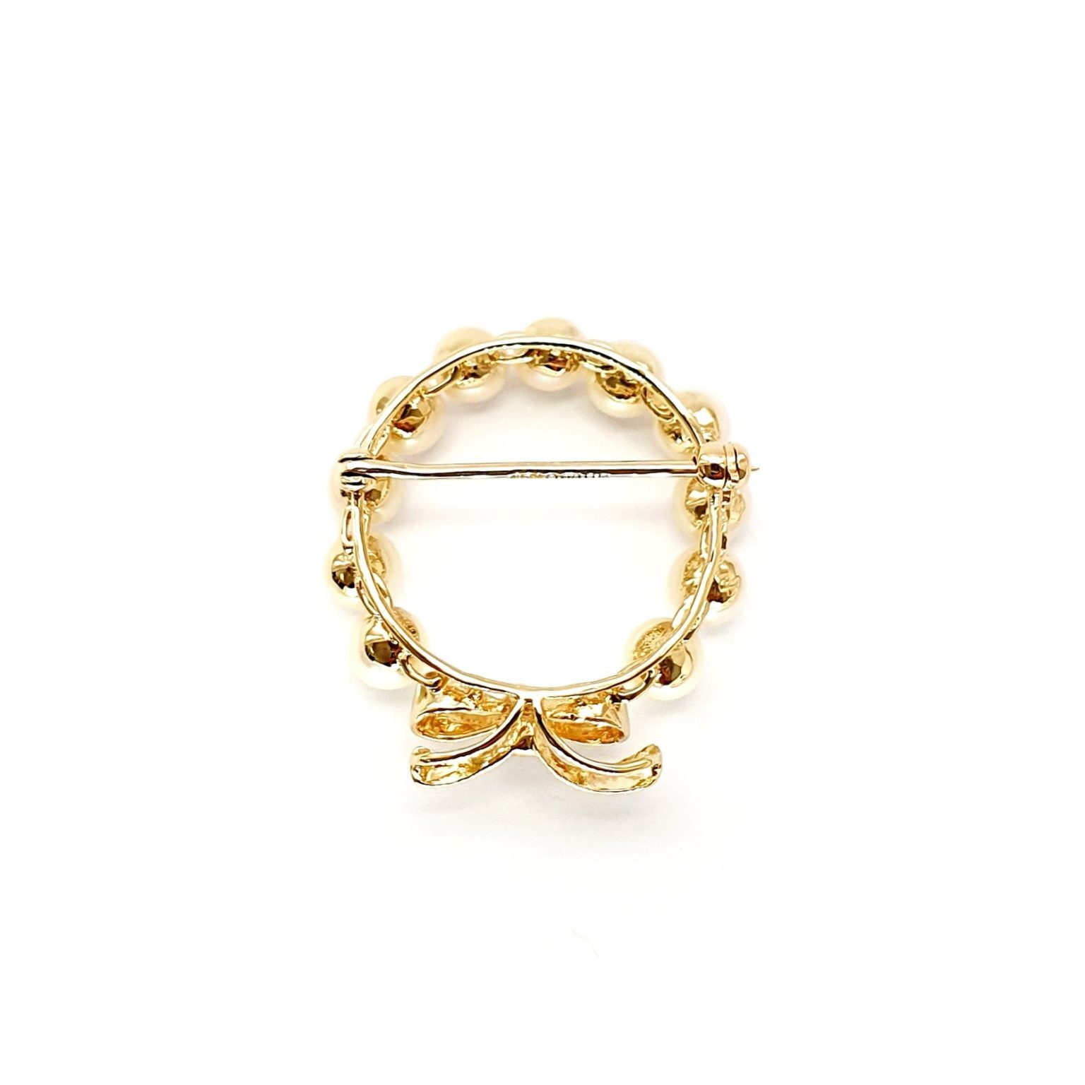 A 9ct yellow gold brooch with a circle of eleven 5mm round pearls leading to a bow to the bottom with three petite round diamonds set to the centre of the bow. Showing back view.