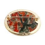 This stunning brooch features a domed oval moss agate stone semi-translucent, exhibits captivating dendritic inclusions. As a result, the stone displays mesmerizing swirls of orangish-red and deep green., exquisitely set in a 9ct yellow gold rub-over setting it is framed by twisted gold wire and includes an open-back bezel to maximizes light exposure. Back view showing the pin.