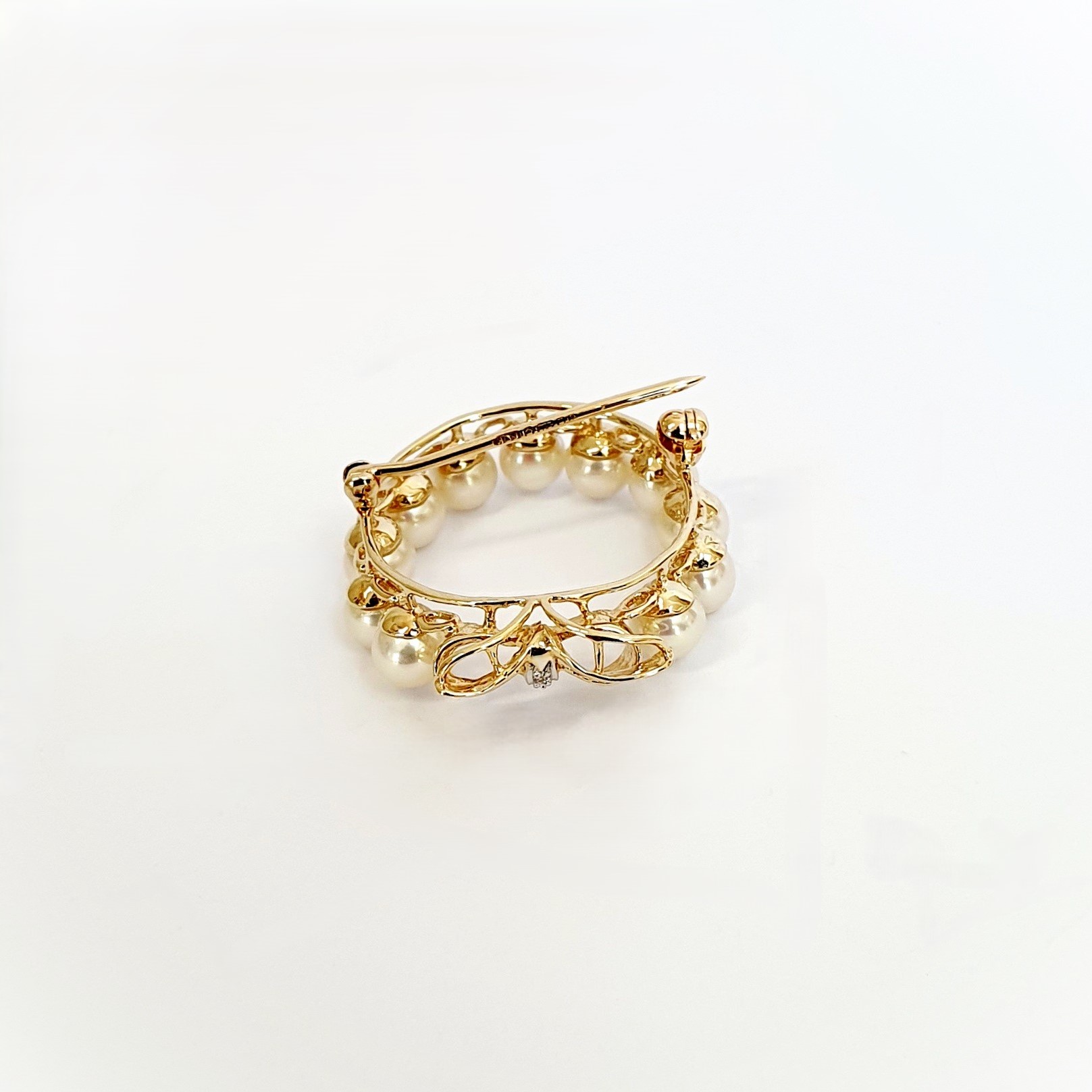 A 9ct yellow gold brooch with a circle of eleven 5mm round pearls leading to a bow to the bottom with three petite round diamonds set to the centre of the bow. Showing side view.