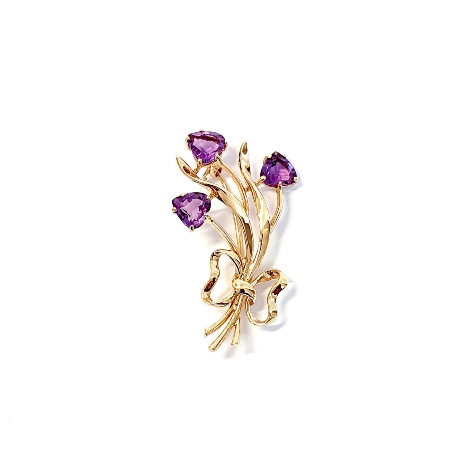Crafted in 9ct yellow gold with three stems of purple amethyst hearts as flowers with leaves & a golden bow