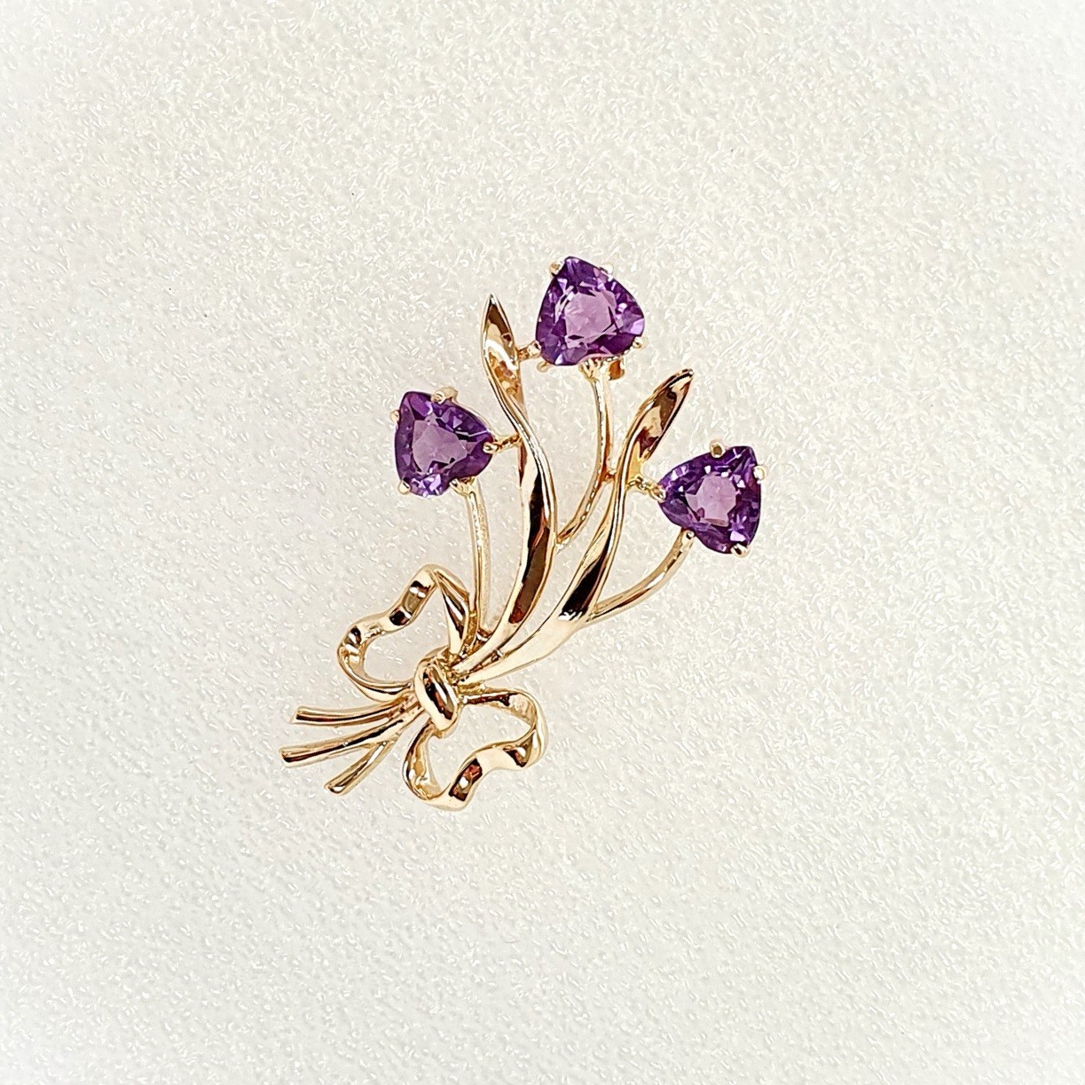Crafted in 9ct yellow gold with three stems of purple amethyst hearts as flowers with leaves & a golden bow