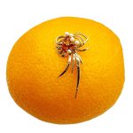 This gorgeous multi-loop bow brooch is crafted in 9ct yellow gold and features three golden yellow Citrines and five white pearls. Pictured on an orange.