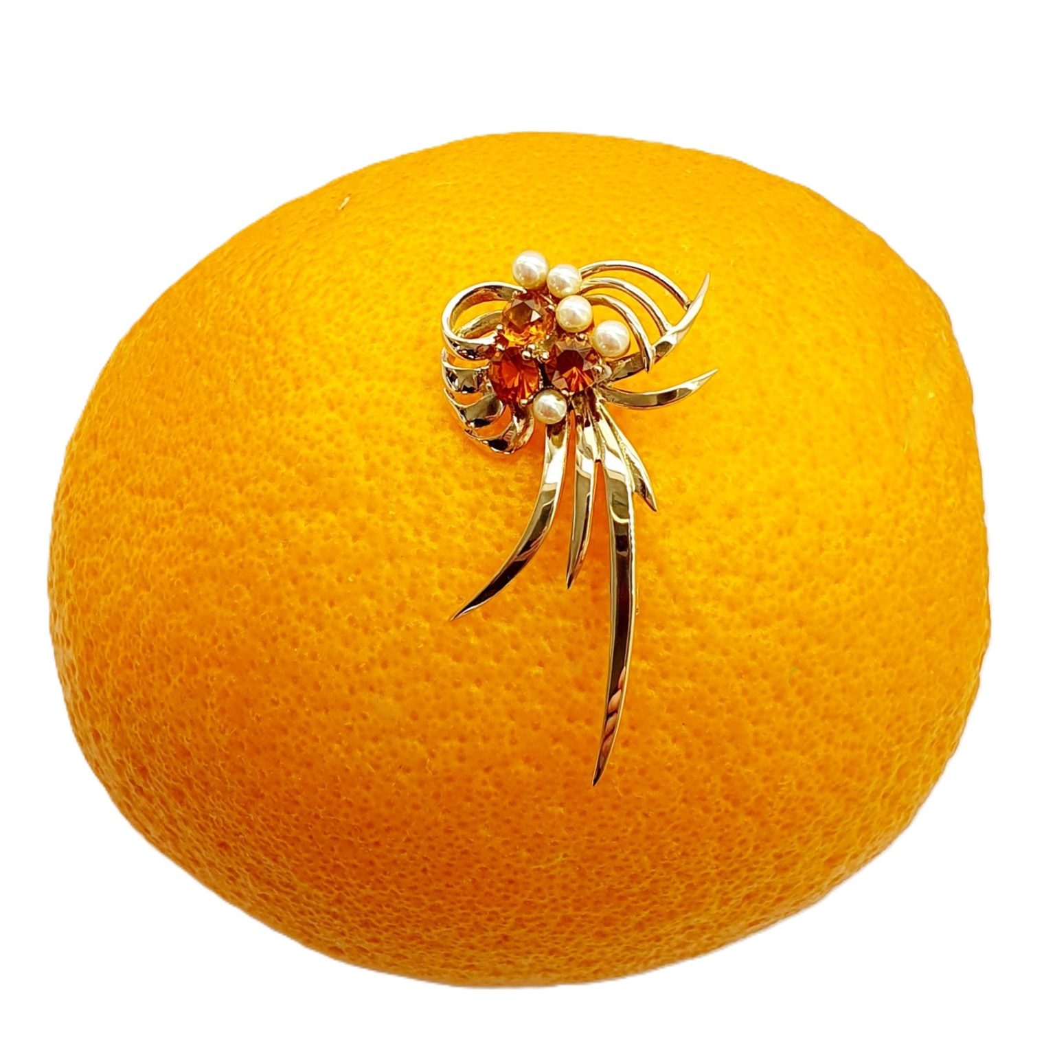 This gorgeous multi-loop bow brooch is crafted in 9ct yellow gold and features three golden yellow Citrines and five white pearls. Pictured on an orange.