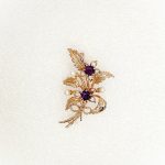 9ct rose gold flower brooch with five leaves, two round purple amethyst stones and three pearls made into a bouquet and tied to the bottom with a small twisted gold bow. Front view.