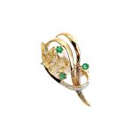 9ct yellow gold brooch with a sprig of seven leaves coming through a floral swirl of polished and barked yellow gold with three bright green emeralds & three sparkling diamonds set into a small white rhodium section, top view.