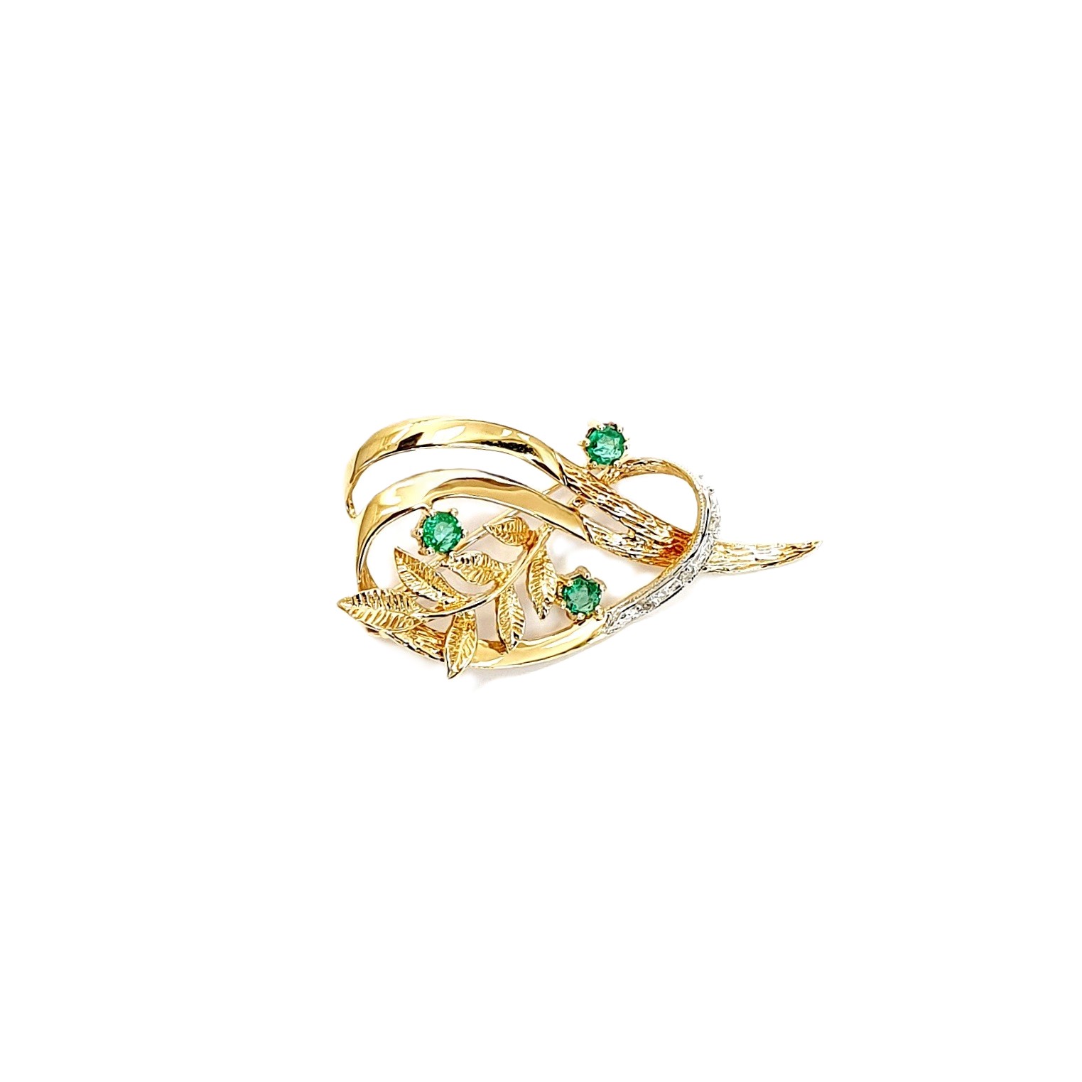9ct yellow gold brooch with a sprig of seven leaves coming through a floral swirl of polished and barked yellow gold with three bright green emeralds & three sparkling diamonds set into a small white rhodium section, top view.