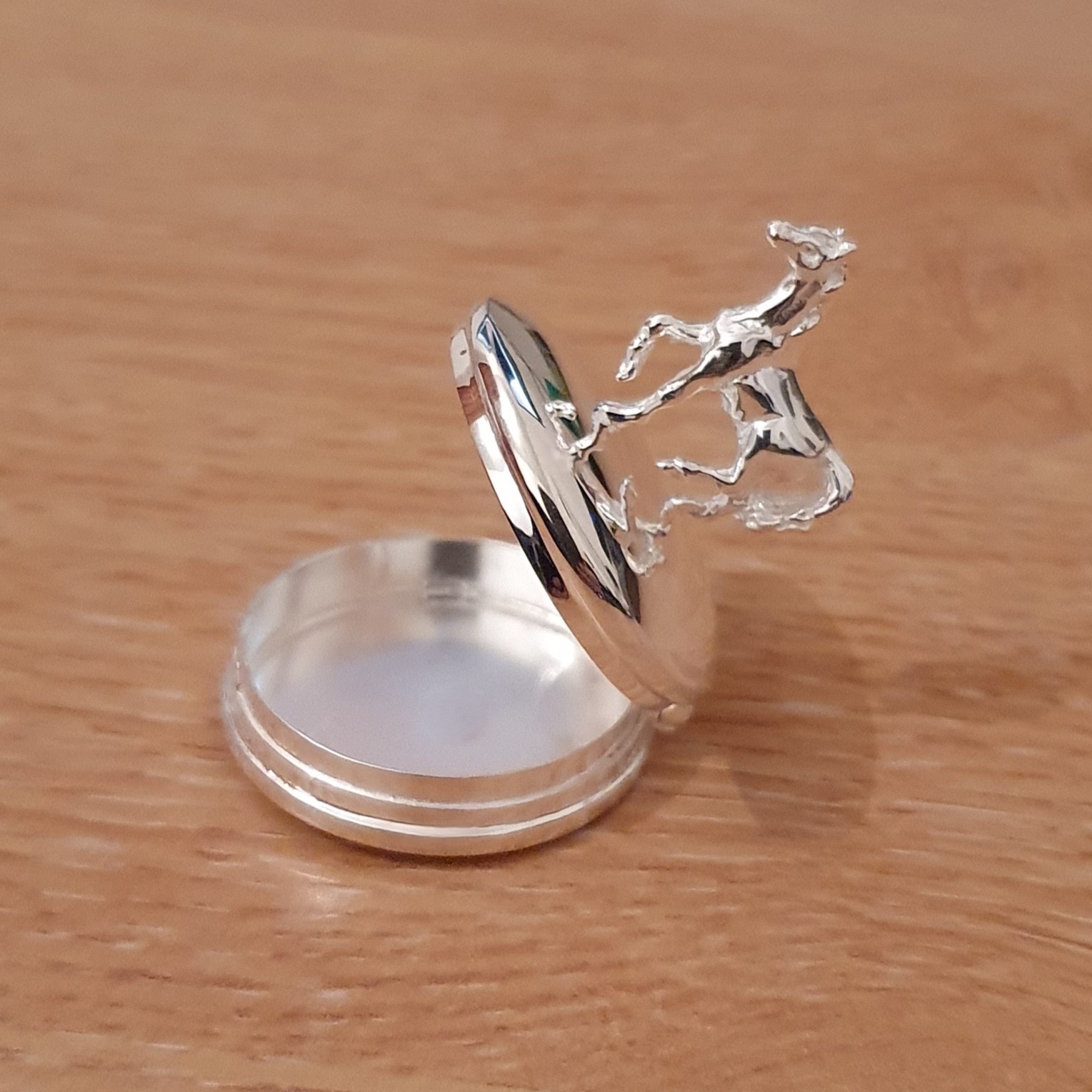A petite round polished silver trinket box with a cantering horse on the top of the hinged lid.Open.