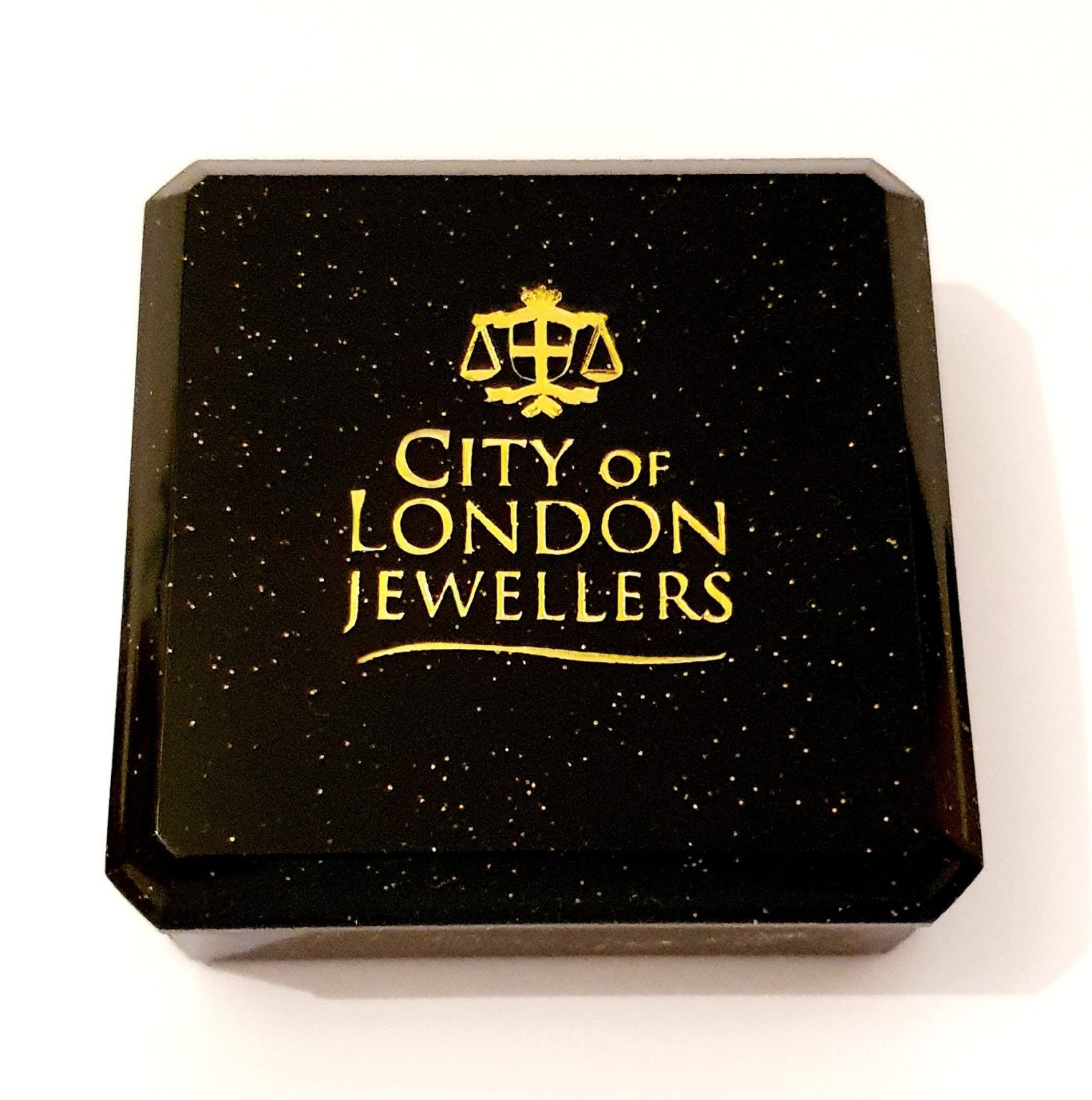 Black with gold speckles plastic box with cotton wool inside. Closed.