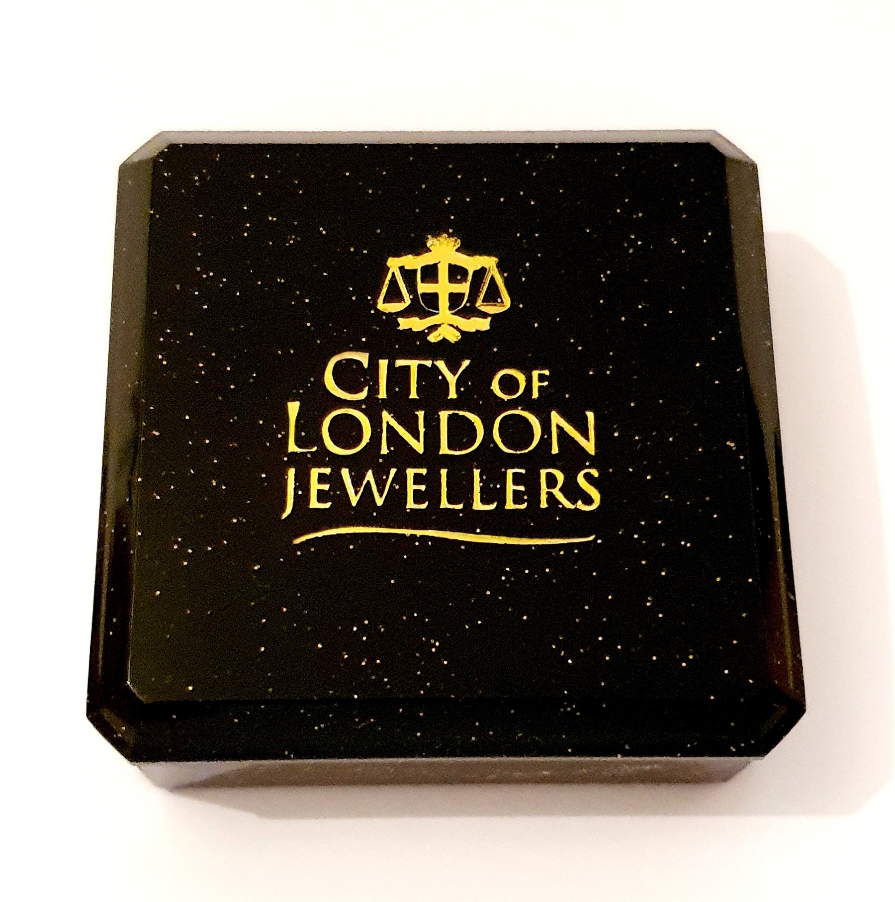 Black with gold speckles plastic box with cotton wool inside. Closed.