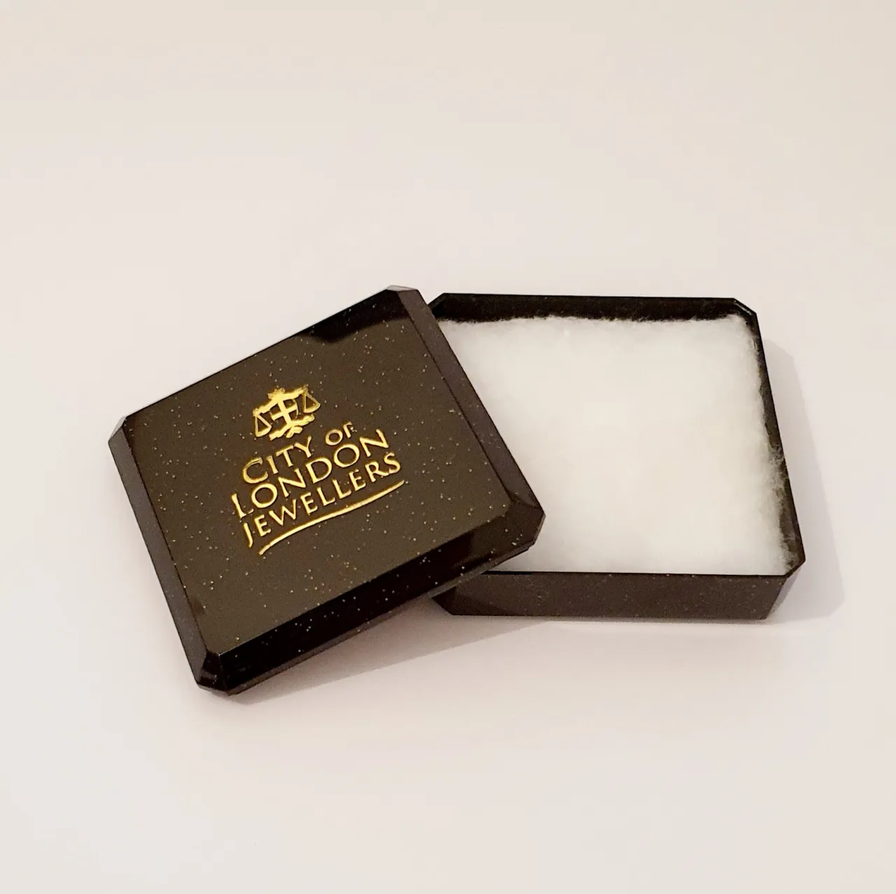Black with gold speckles plastic box with cotton wool inside. Open.