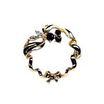 Yellow gold round ribbon with three round dark blue sapphire and two diamond leaves with a bow to the bottom centre. Pictured close up.