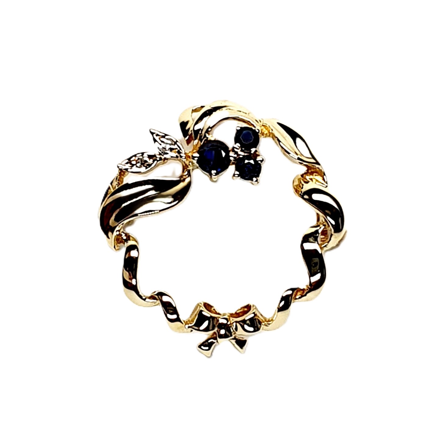Yellow gold round ribbon with three round dark blue sapphire and two diamond leaves with a bow to the bottom centre. Pictured close up.