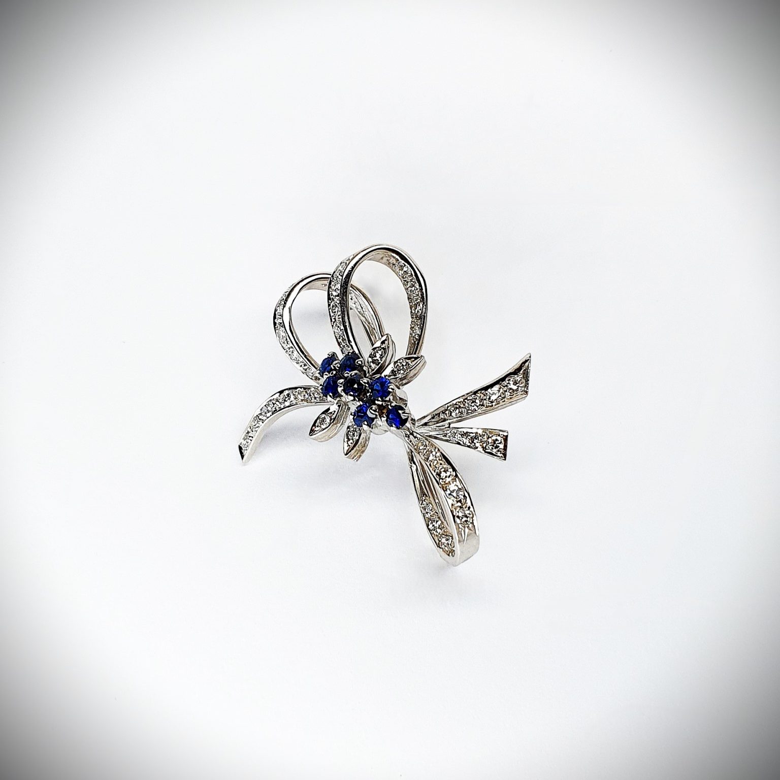 Angled View "An angled shot of the Cropp & Farr brooch, capturing the sparkling sapphires and diamonds, and the graceful curves of the bow design. Stock number: BRQ00050."