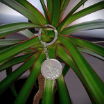 Front view on a plant: "Silver Saint Christopher keyring elegantly displayed against vibrant green leaves, highlighting its craftsmanship and design."