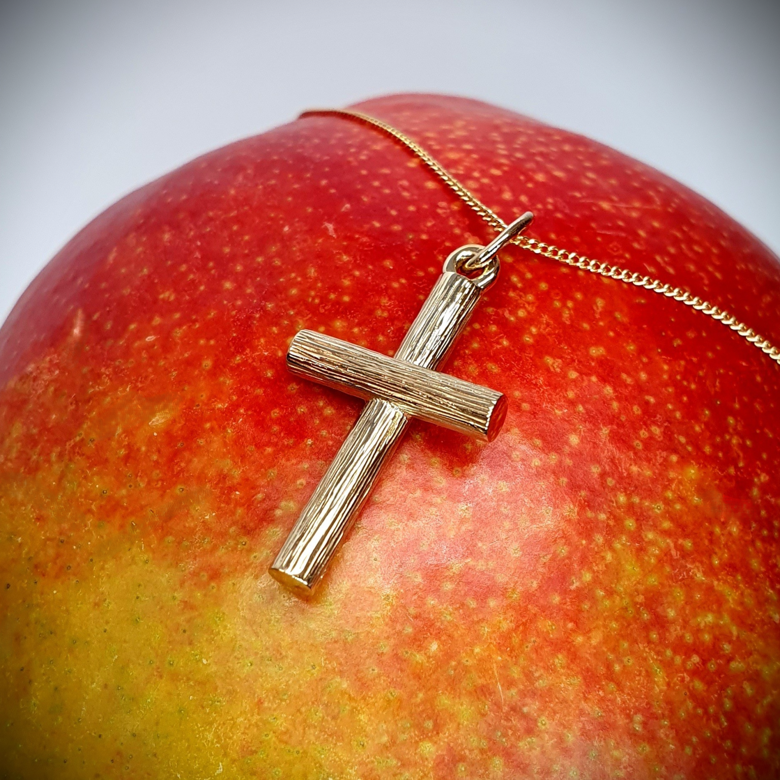9 karat gold cross pendant with bark texture resting on mango, angled to the right