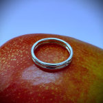 Wedding ring positioned on a mango with vibrant blue backdrop — the ring’s polished surface gleams against the mango’s golden skin, set against a bright blue background for bold, tropical contrast.