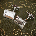 Diamond Rectangular Sterling Silver Cufflinks against a green book background: Hoxton cufflinks with a simple curved rectangular design and diamond accent in a square box setting, showcased against a black background.