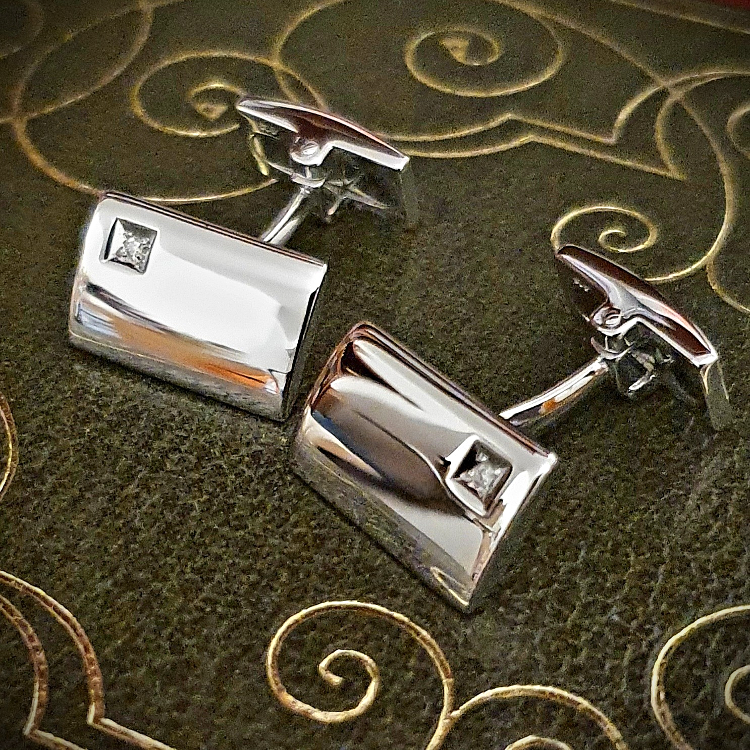 Diamond Rectangular Sterling Silver Cufflinks against a green book background: Hoxton cufflinks with a simple curved rectangular design and diamond accent in a square box setting, showcased against a black background.
