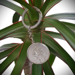 Front view on a plant: "Silver Saint Christopher keyring elegantly displayed against vibrant green leaves, highlighting its craftsmanship and design."