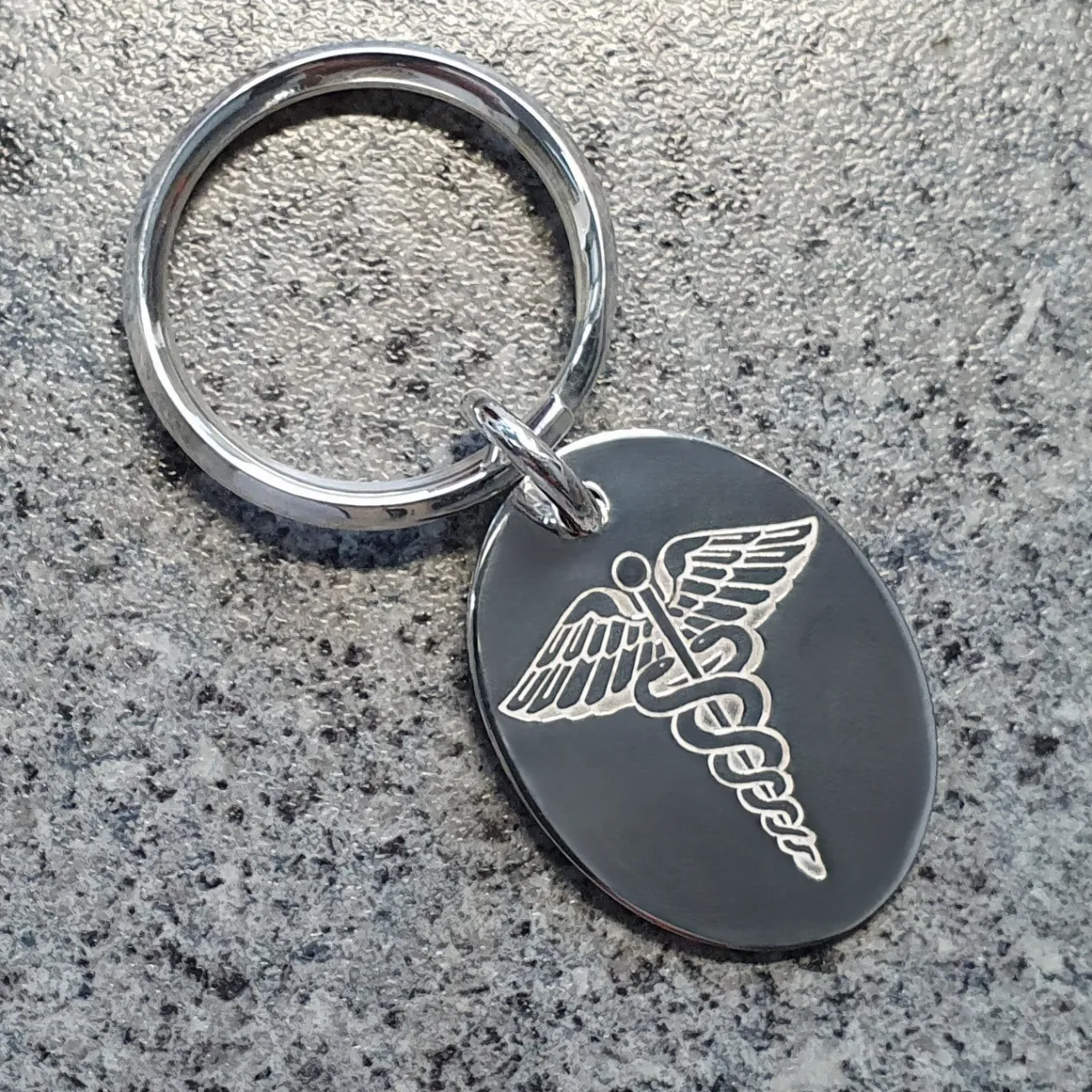 Medic Alert Tag on a key fob in solid silver on granite background.
