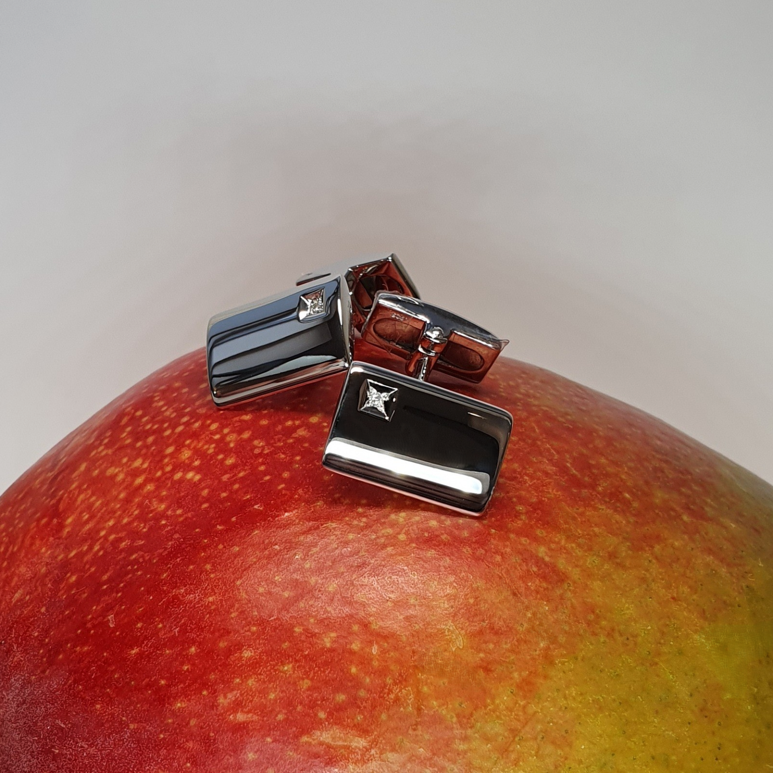 Elegant Hoxton Cuff Link fasteners with a curved rectangular design and a 1mm round diamond in a square box setting, resting on a mango.