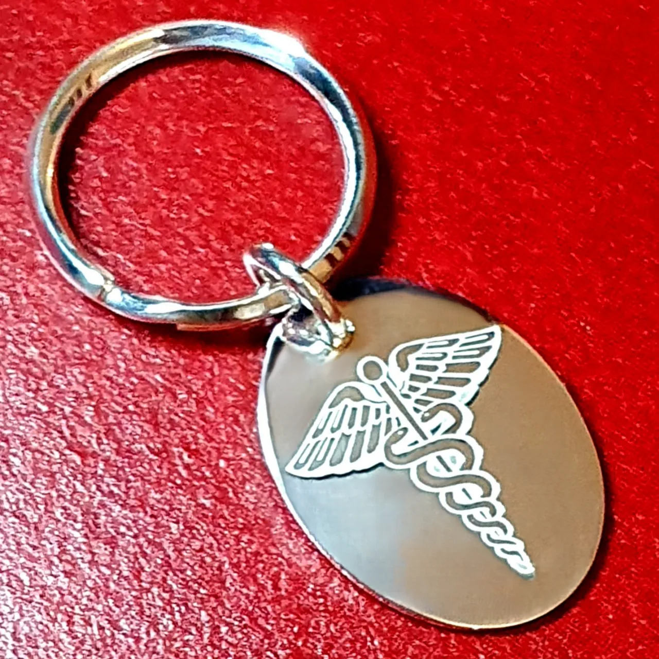 close up photo of a Medic Alert Tag on a key fob in solid silver pictured on a red back ground.