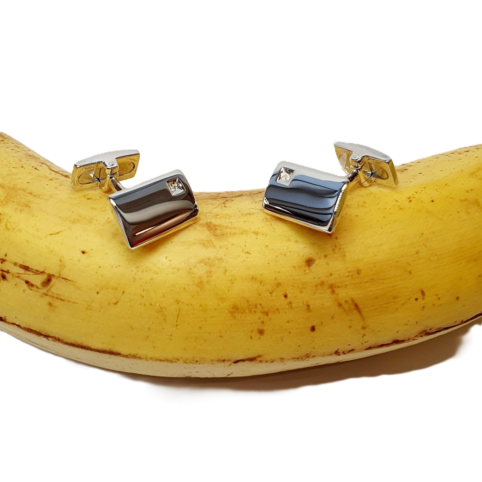 Elegant Hoxton Sleeve fasteners with a curved rectangular design and a 1mm round diamond in a square box setting, resting on a banana.