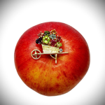 Front View 1: This is an image of the front of the 9ct Gold Gemstone Wheel Bow Brooch pictured on an apple. It displays the amethyst, blue topaz, citrine, garnet, peridot, and tourmaline set in yellow gold.