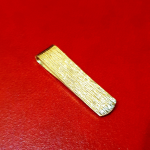Tree-barked patterned money clip in 9ct gold pictured on a red back ground.