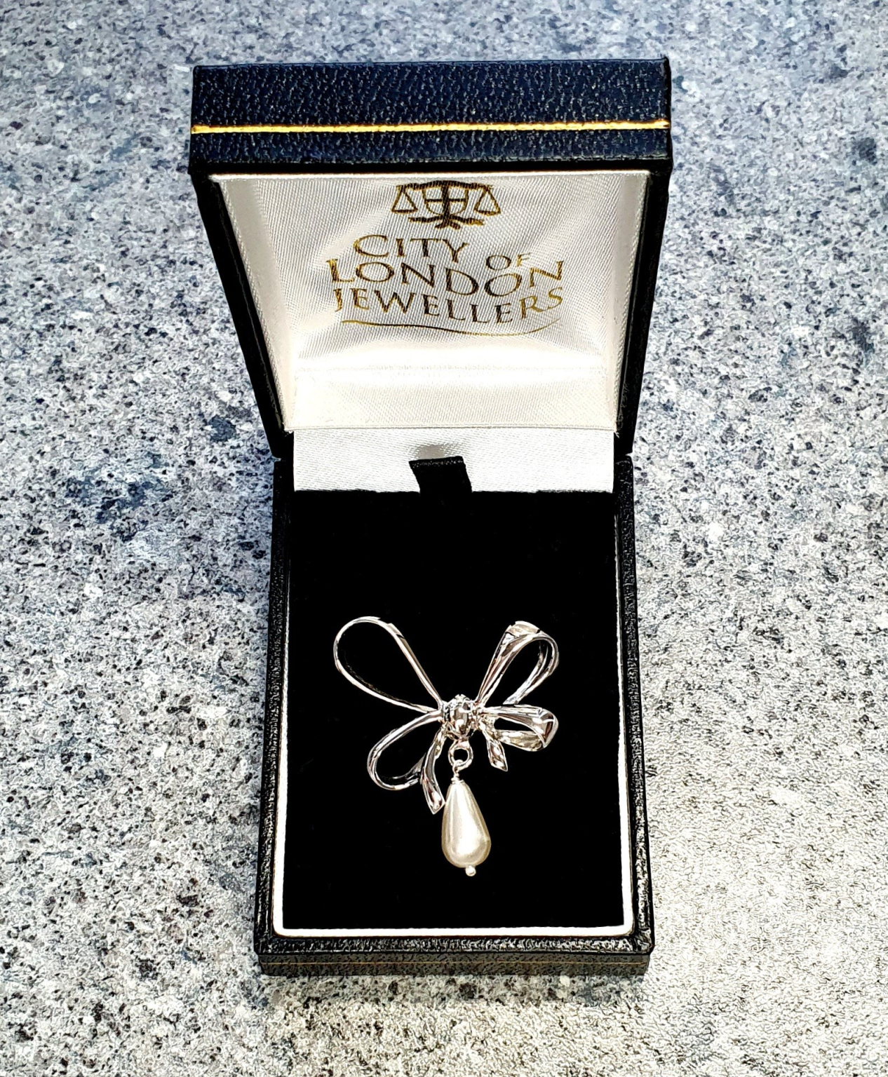 An elegant bow-shaped brooch displayed in a sleek black presentation box with velvet padding.
