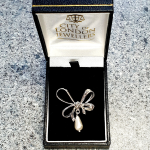 An elegant bow-shaped brooch displayed in a sleek black presentation box with velvet padding.