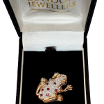 Broche grenouille en or jaune et blanc avec des rubis rouges et des diamants blancs.