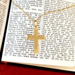 Lord's Prayer etched on the front of a genuine gold cross pendant and chain pictured on an open bible.
