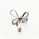 A stunning bow-shaped brooch on a white background, emphasizing its detailed craftsmanship and central teardrop pearl.