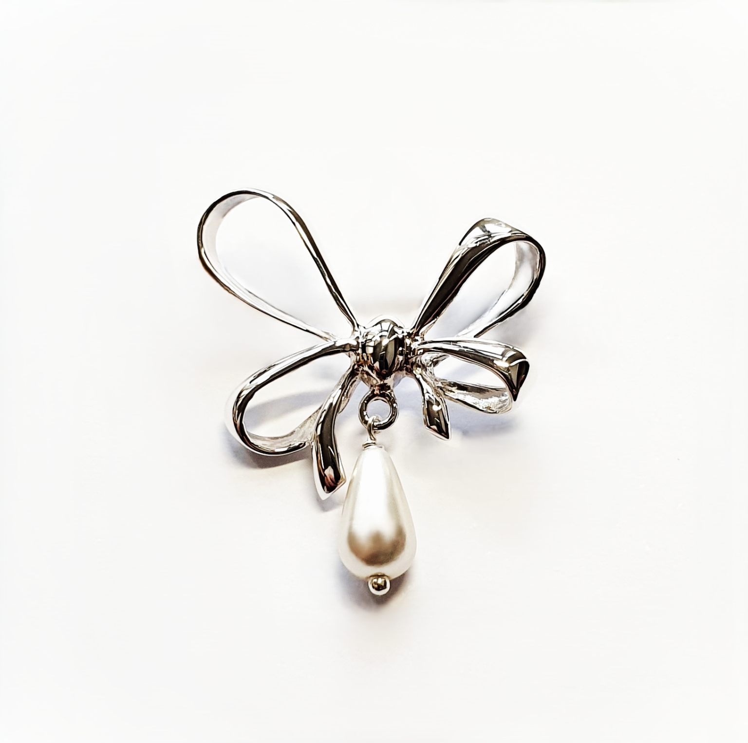 A stunning bow-shaped brooch on a white background, emphasizing its detailed craftsmanship and central teardrop pearl.