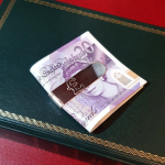 The front of this genuine silver money clip is pictured with a twenty-pound note sitting on a green book.