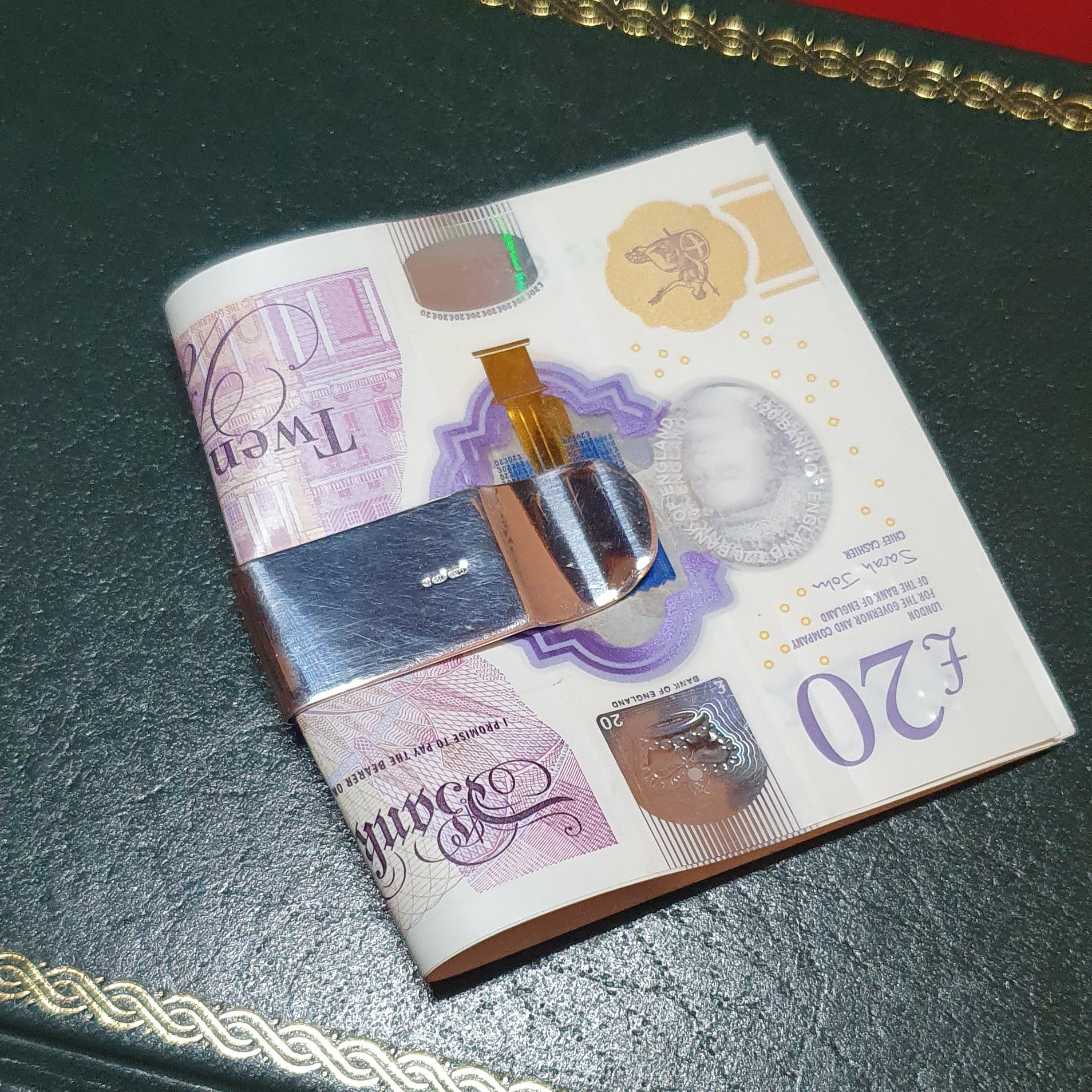 The plain polished back of the clip is shown with a 20-pound note pictured on a green book.