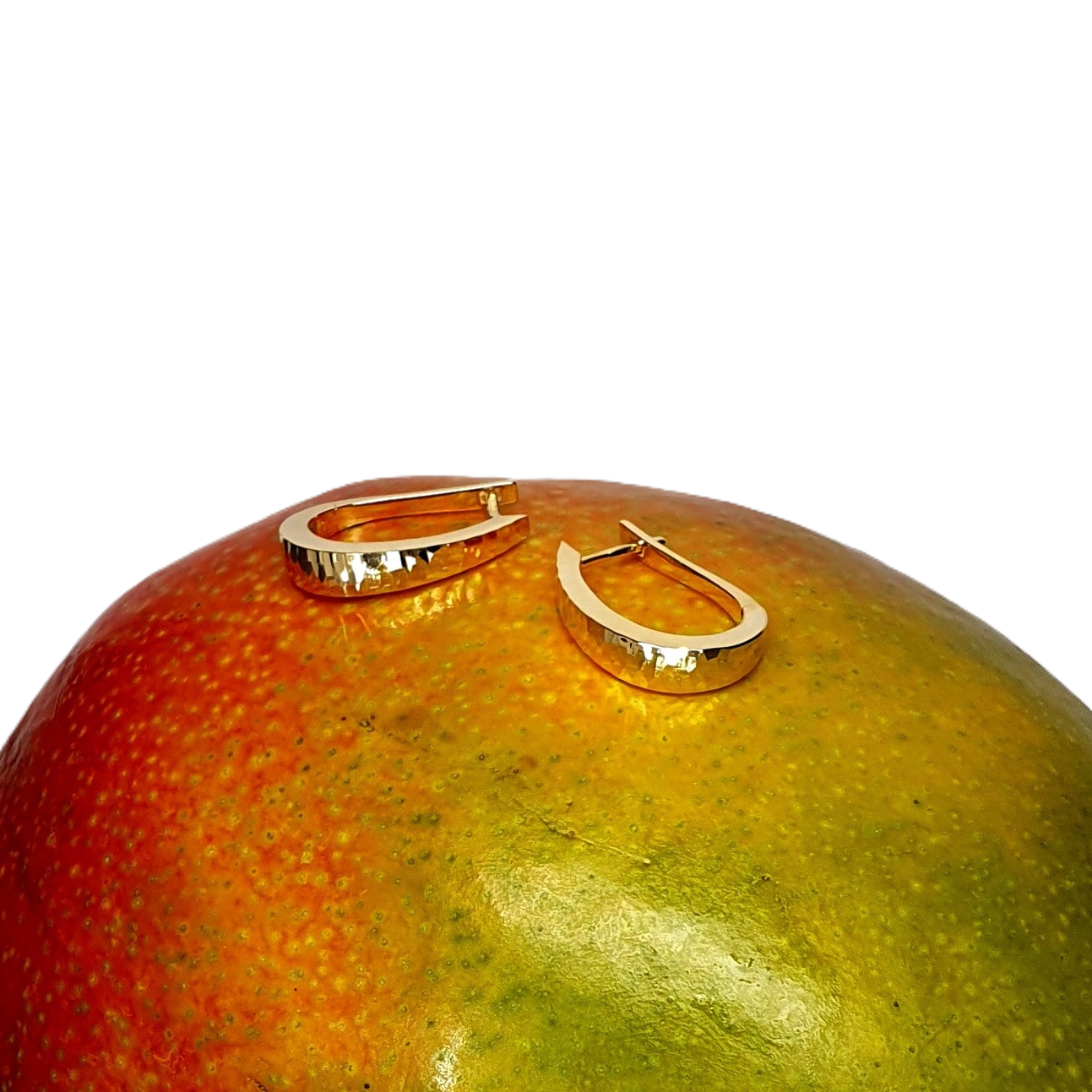 Diamond-cut hoop earring pictured laying flat on top of a mango for contrast.
