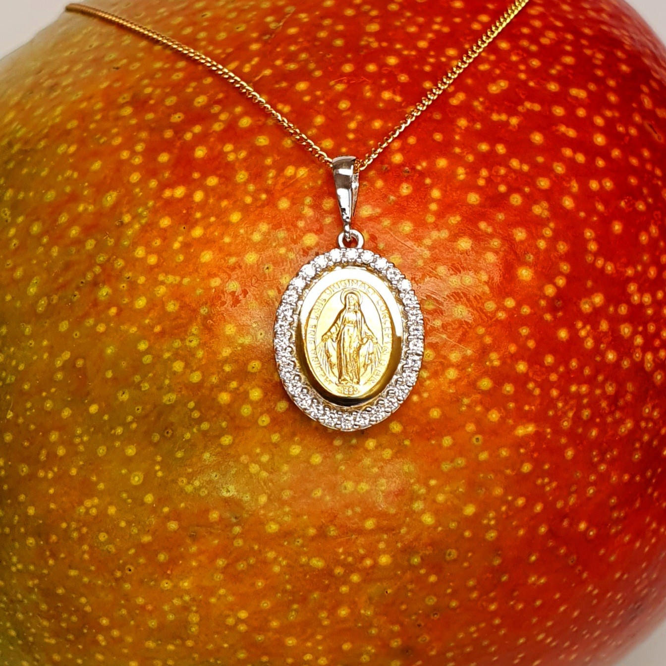 Hallmarked 9-carat yellow & white gold oval Miraculous necklace with a cubic zirconia border PC00557 is surrounded by a cubic zirconia border—the front view is pictured on a mango.
