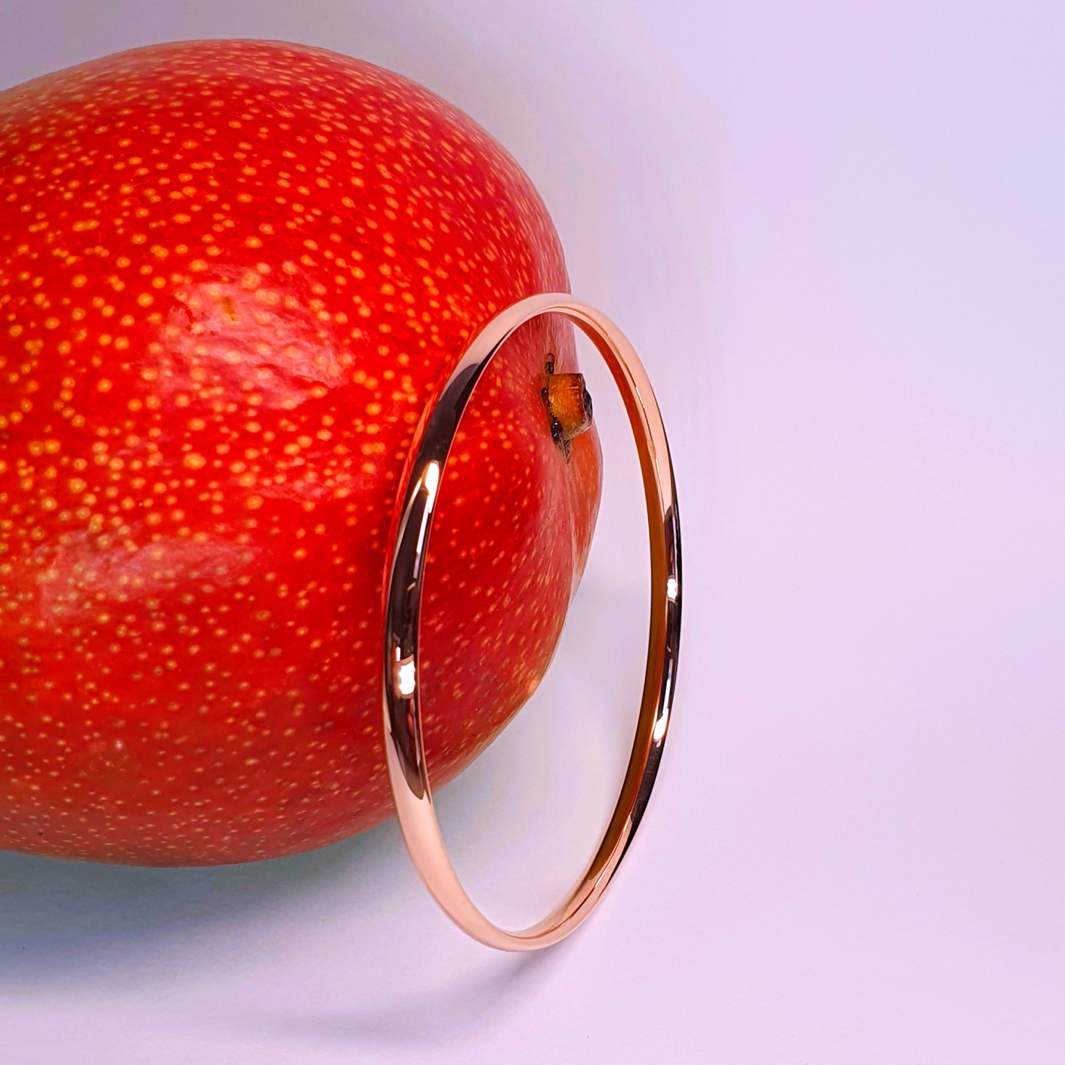 Red gold court shape bangle pictured with a mango.