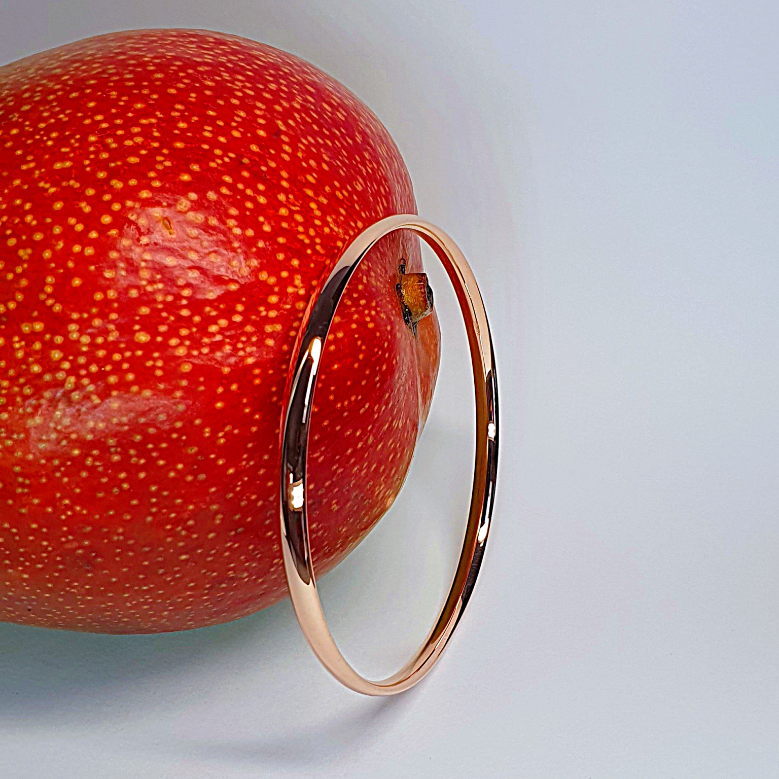 Pink gold court shape bangle pictured with a mango.