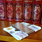Genuine silver twin cash clip pictured at an angle on a bookshelf holding £20.00 notes with red books.