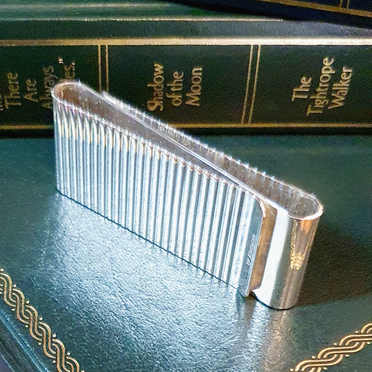 Washboard design, sterling silver, two-sided cash clip pictured on green books showing the edge.