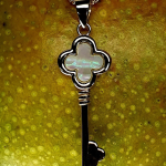 A 9ct gold pendant shown in extreme close-up against the textured surface of a ripe mango, emphasizing the pendant’s smooth polish and the radiant, multicoloured shimmer of the mother of pearl centrepiece.