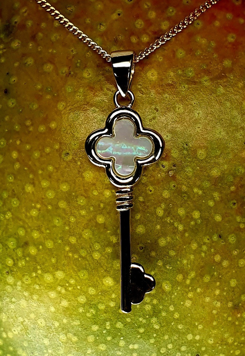 A 9ct gold pendant shown in extreme close-up against the textured surface of a ripe mango, emphasizing the pendant’s smooth polish and the radiant, multicoloured shimmer of the mother of pearl centrepiece.