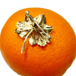 This is a picture of the back of the leaf brooch showing the polished finish and the pin and swivel safety catch pictured on an orange.