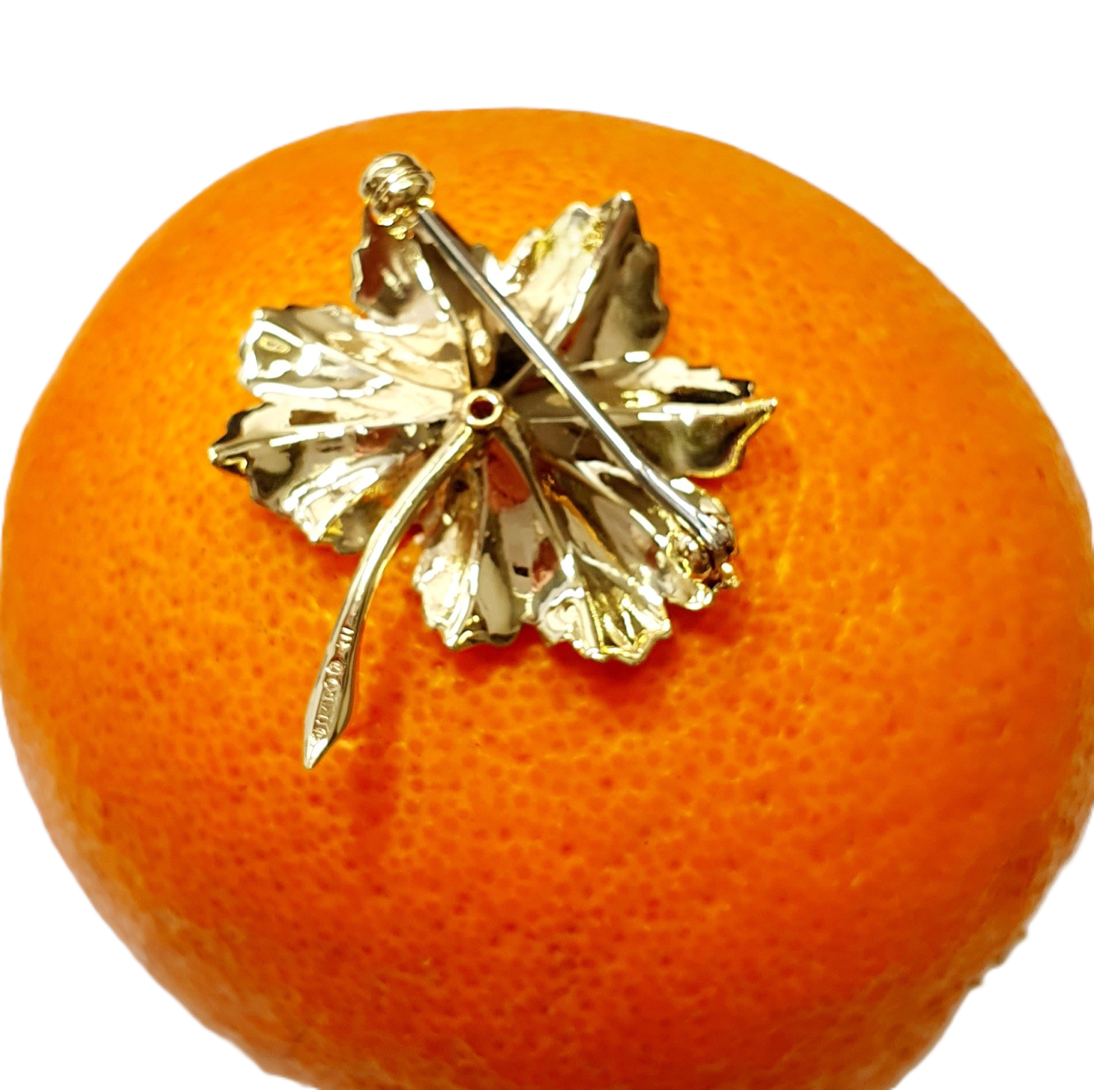 This is a picture of the back of the leaf brooch showing the polished finish and the pin and swivel safety catch pictured on an orange.